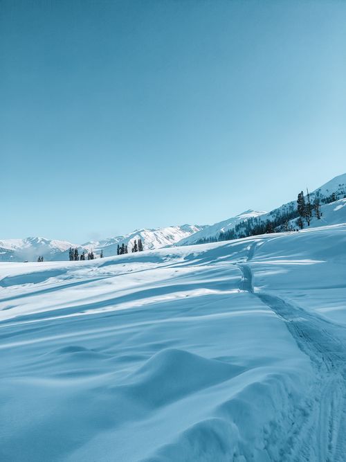 Free A serene winter landscape showcasing snow-covered fields and distant mountains under a clear blue sky. Stock Photo