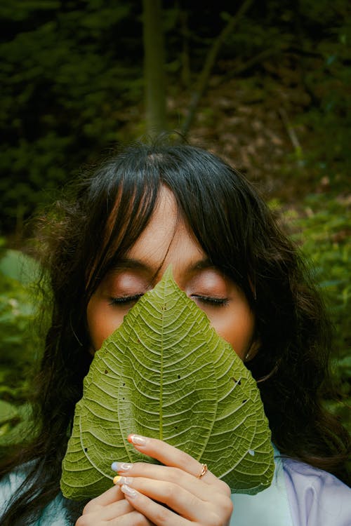 A Woman Covering Her Face With Green Leaf