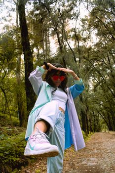 Stylish woman in sunglasses and denim poses on a forest trail, showcasing fashion and nature.