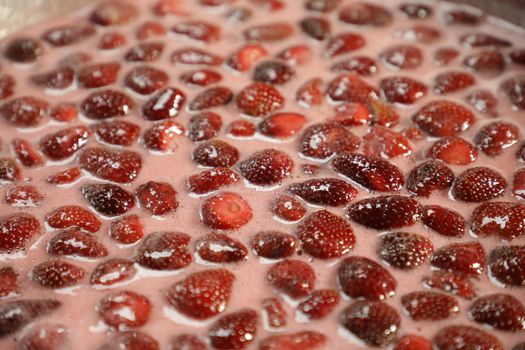 A close-up shot of fresh strawberries soaking in syrup, capturing their juicy texture.