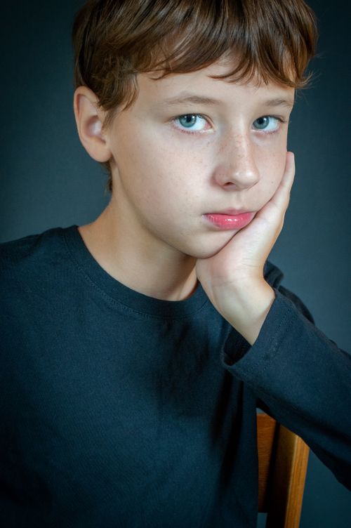 Free A young boy with blue eyes poses pensively, resting his hand on his cheek in a studio portrait. Stock Photo