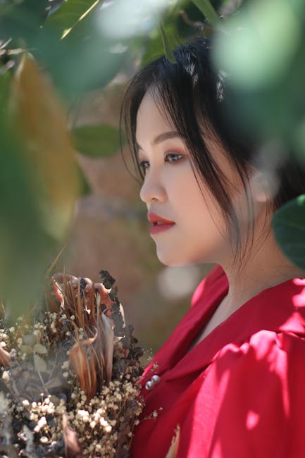 Profile portrait of an East Asian woman in a red dress, surrounded by nature. Soft focus and warm tones.