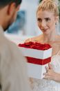 Woman in White Floral Lace Wedding Dress Holding Red and White Gift Box
