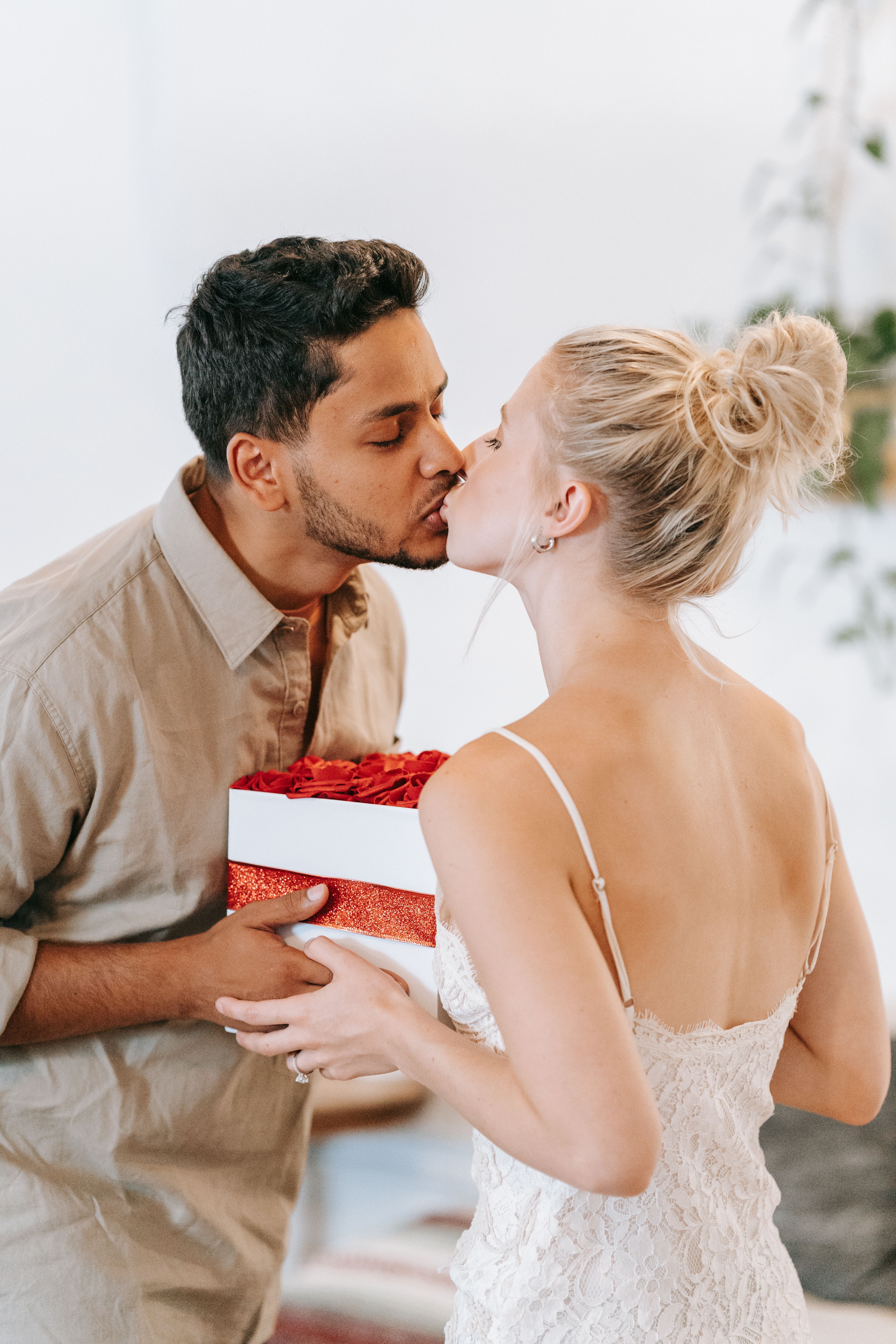 A couple shares a kiss while exchanging a gift in an indoor setting.