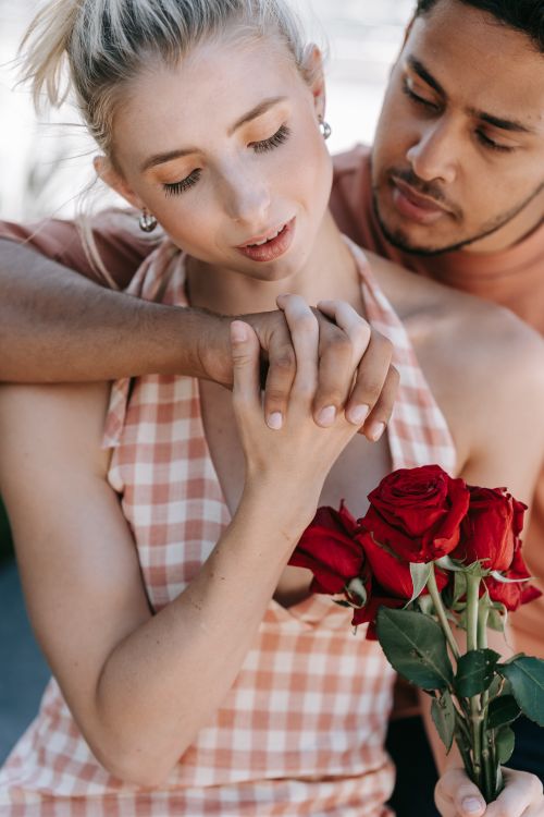 Free A romantic scene of an interracial couple holding hands with red roses, expressing love and intimacy. Stock Photo