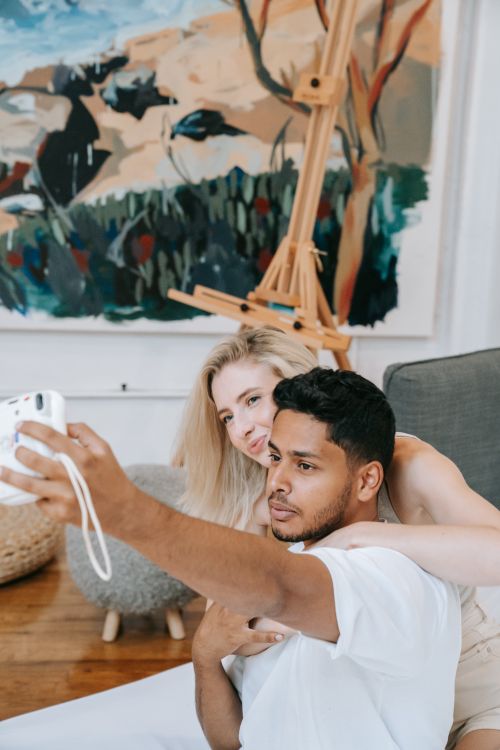 Free A loving couple takes a cheerful selfie in a cozy art studio setting, embracing creativity. Stock Photo