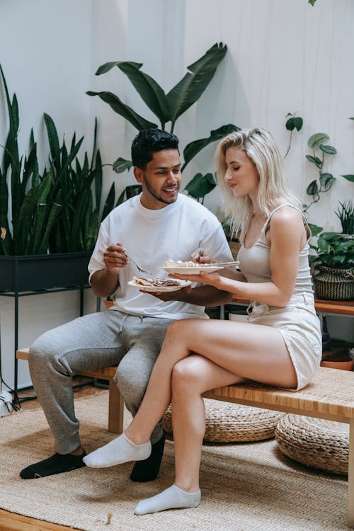 Man and Woman Holding Food on Plate While Sitting on Bench