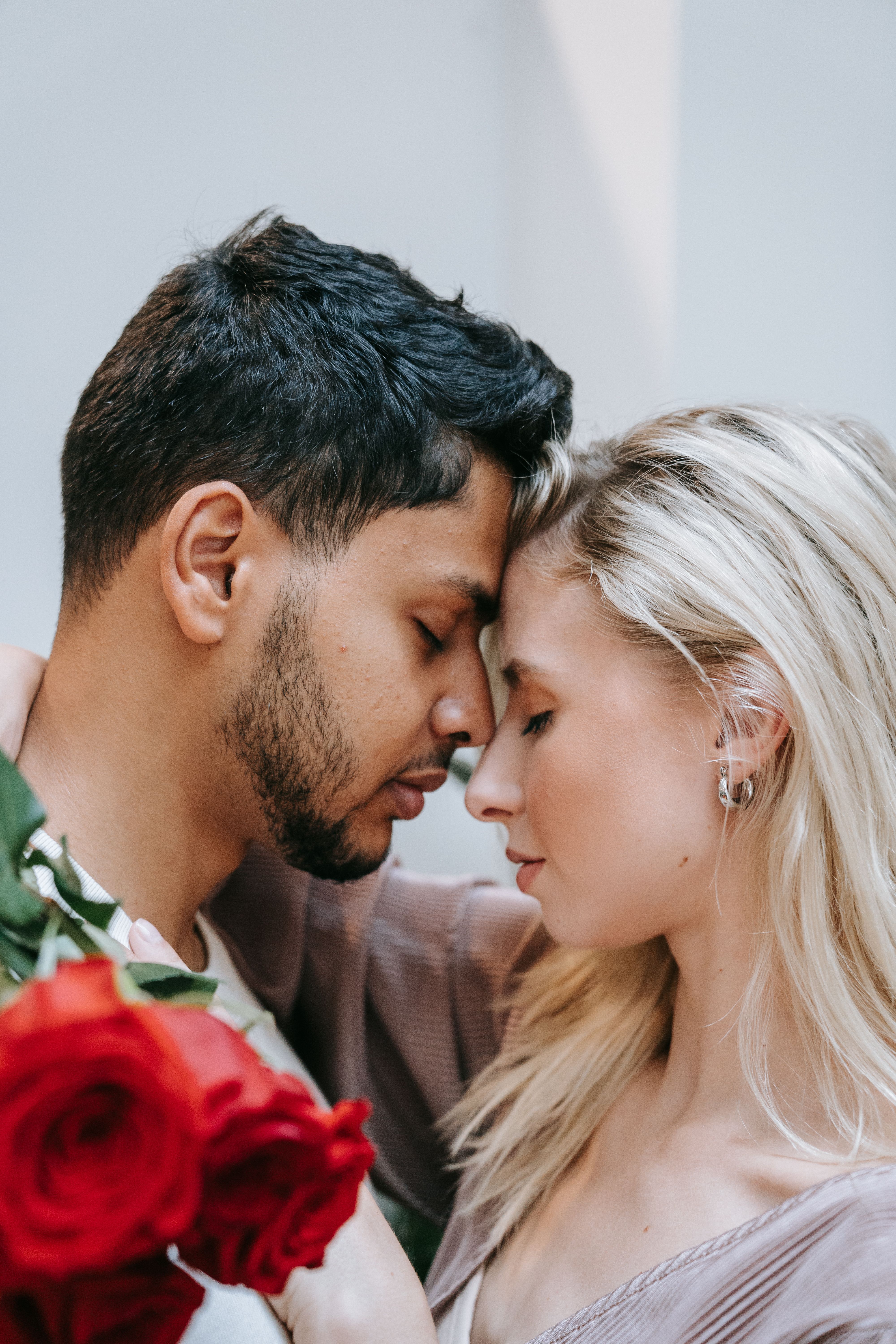Tender moment between an interracial couple indoors with roses, symbolizing love and affection.