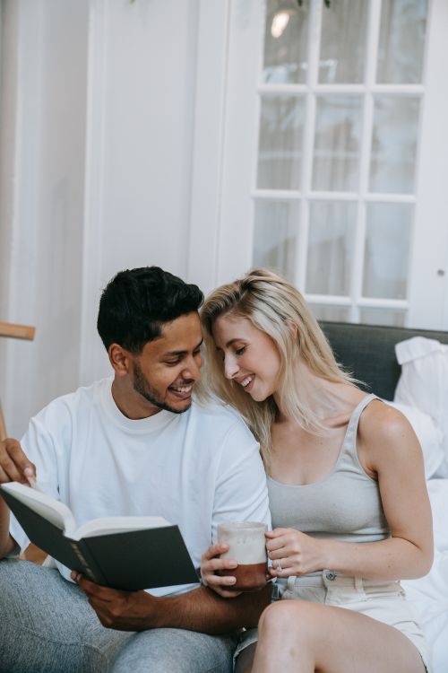 Free A happy couple sitting indoors, sharing a book and coffee, enjoying a cozy moment together. Stock Photo