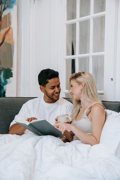 Free A happy interracial couple enjoys reading and coffee in bed, fostering love and connection. Stock Photo
