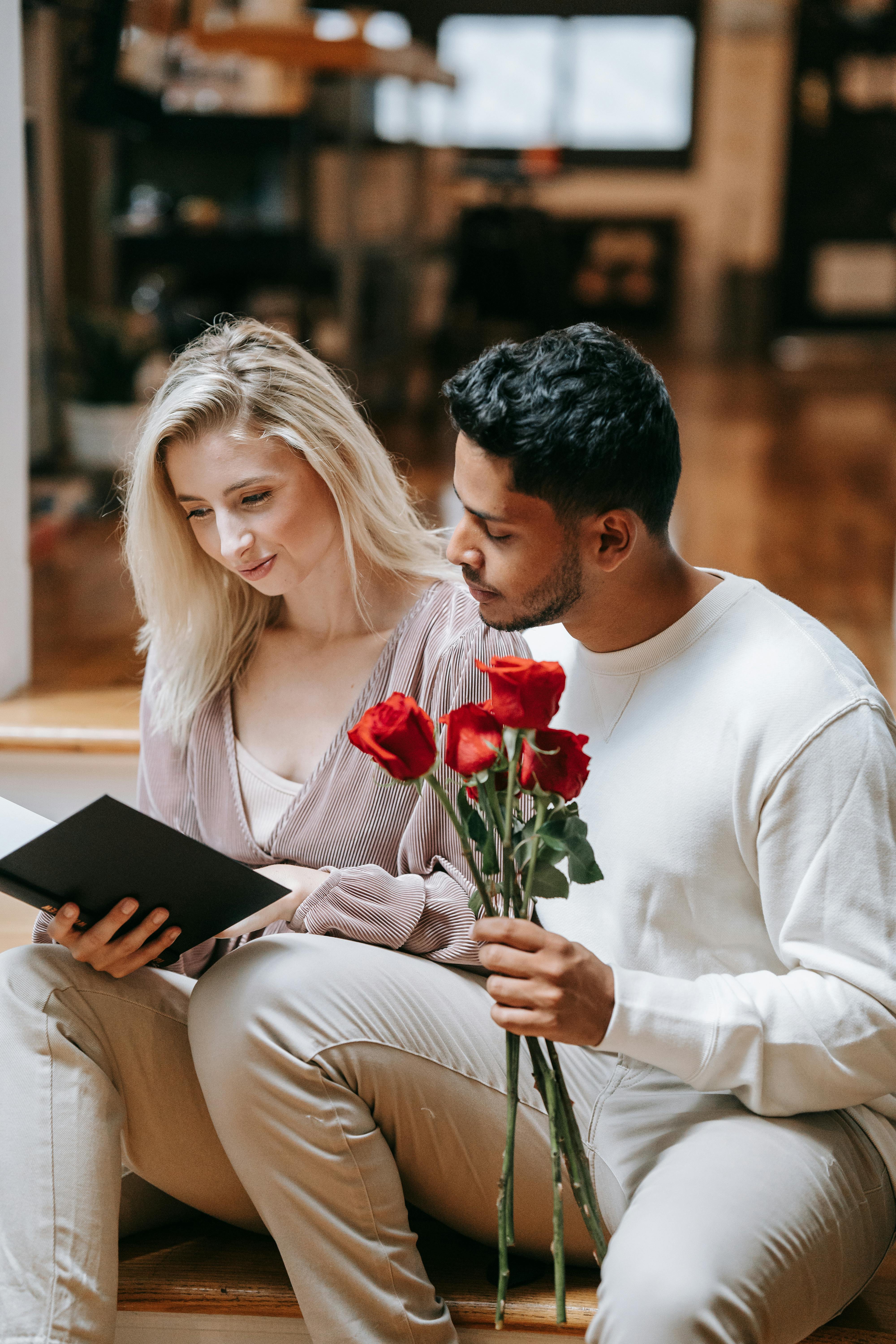 A couple sitting together indoors sharing a special moment with red roses and a tablet, capturing romance and connection.
