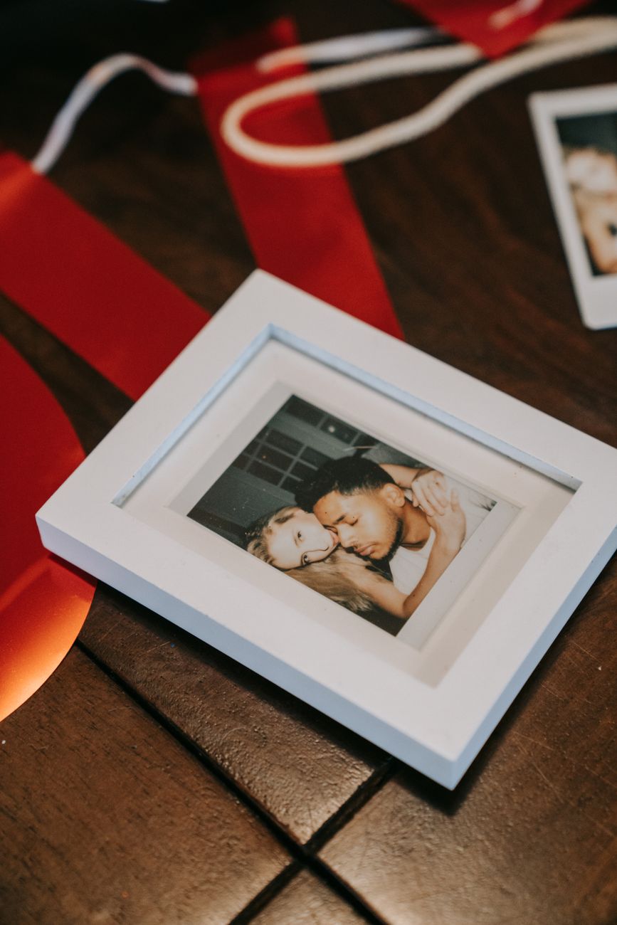 Close-up of a framed polaroid of a couple placed on a wooden table, surrounded by red ribbons.