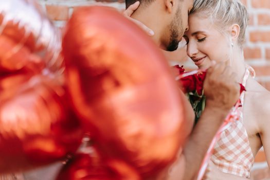 Intimate moment of couple embracing with red balloons and roses outdoors.