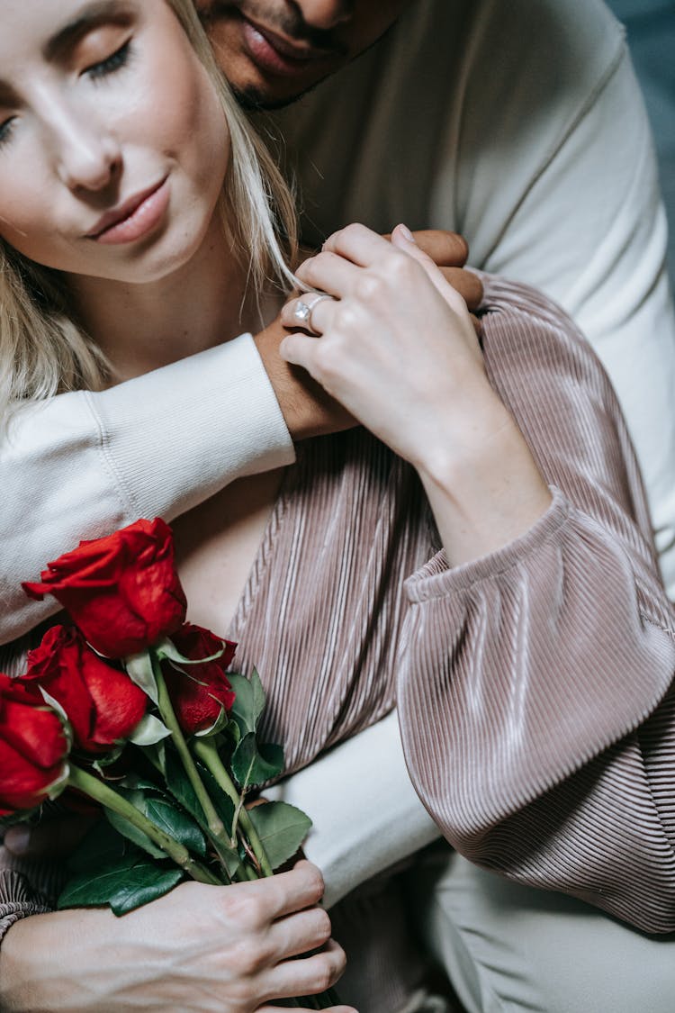 A Man Hugging A Woman Holding Flowers