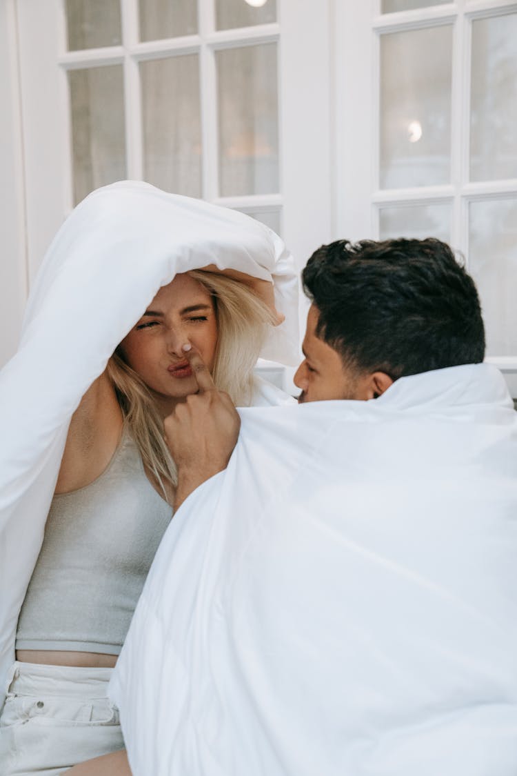 A Woman Pointing At Her Nose While Holding A Blanket Over Her Head