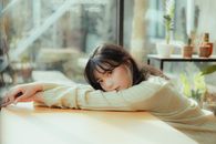 Girl in Beige Long Sleeve Shirt Leaning on Brown Wooden Table