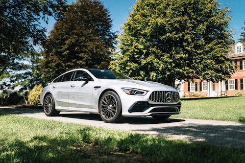 Free A sleek silver Mercedes-Benz GT sedan parked on a driveway surrounded by greenery under a sunny sky. Stock Photo