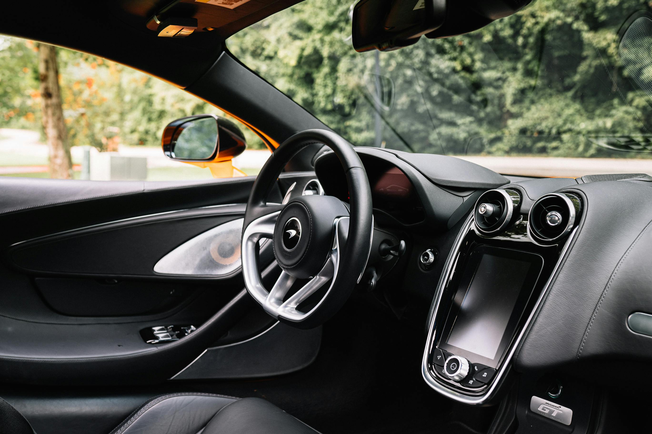 Close-up view of a luxury sports car interior featuring a steering wheel and dashboard against a blurred outdoor background.