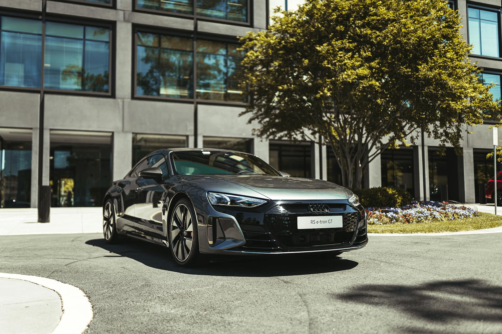 Stunning black Audi RS e-tron GT parked under a tree near a modern building on a sunny day.