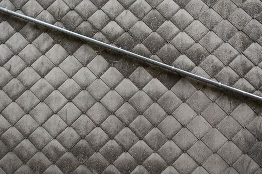 Close-up of a metal pipe on a diamond-patterned concrete wall texture.