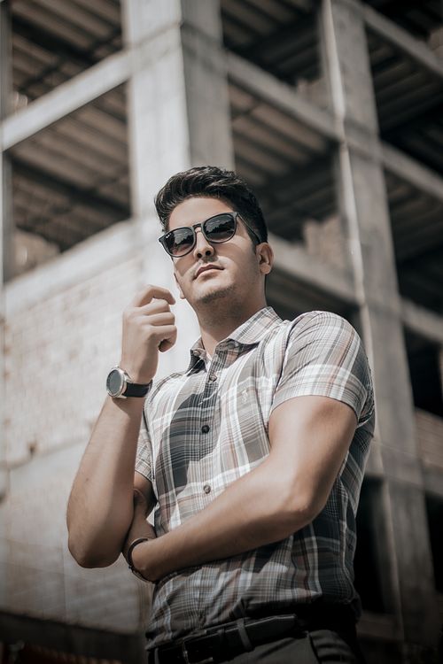 Free Stylish man wearing sunglasses and plaid shirt poses confidently at an urban construction site. Stock Photo