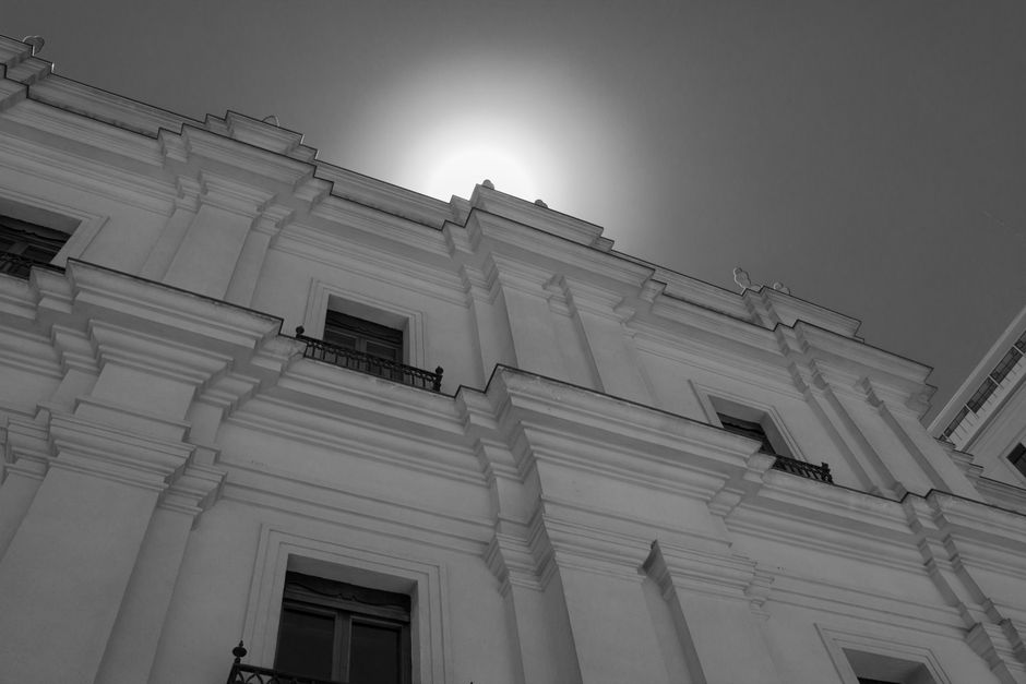 Vista en blanco y negro de una fachada de edificio clásico con la luz del sol proyectando sombras dramáticas.