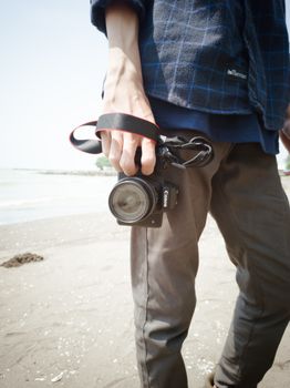 A person holds a camera on a sunny beach, showcasing photography passion.