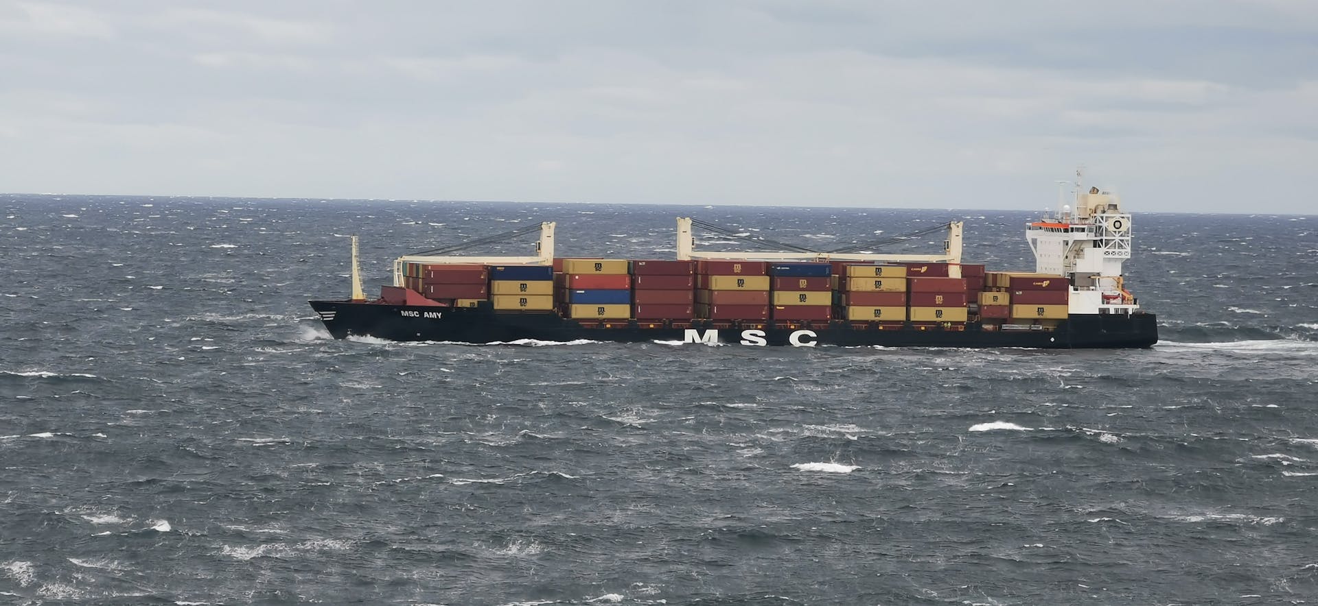 A large cargo vessel transporting containers in the choppy North Sea off the coast of Denmark.