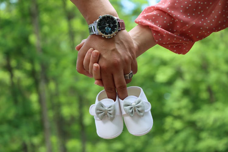 Happy Couple Holding Baby Shoes In Hands