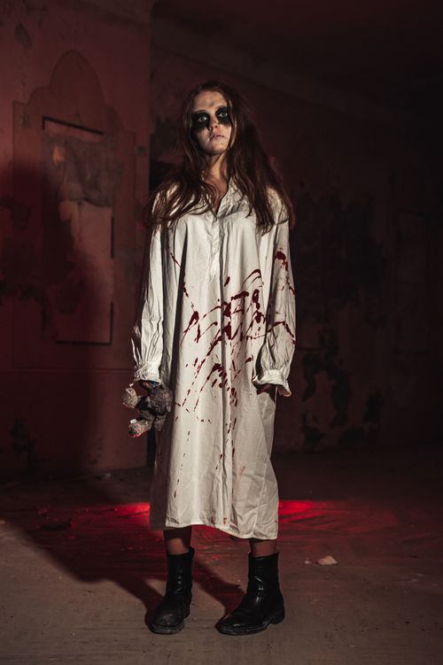 Free A woman in a blood-stained costume stands eerily in a dark, creepy room. Stock Photo
