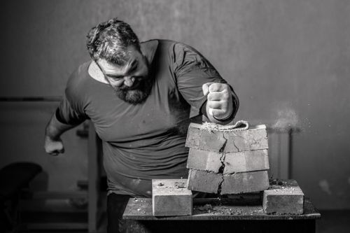Free Powerful image of a man smashing bricks with his fist in a grayscale setting. Stock Photo