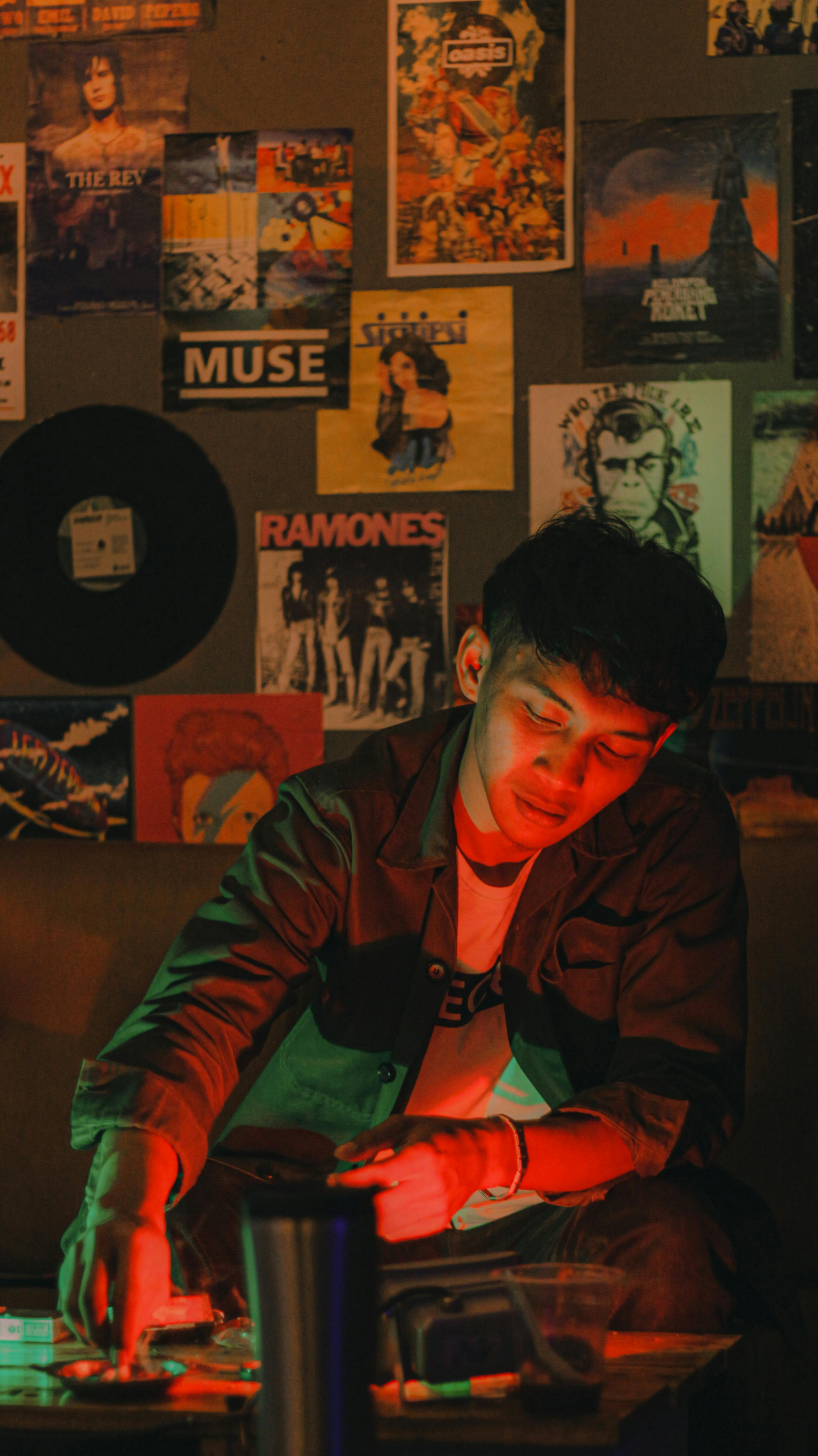 A young man enjoys a relaxed moment in a dimly lit room adorned with vintage music posters.