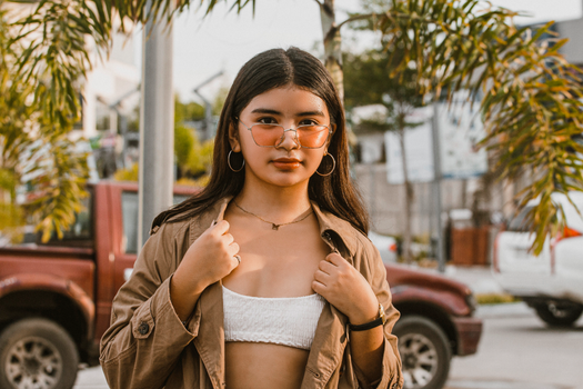 Stylish teenager wearing sunglasses posing confidently outdoors with trees in background.