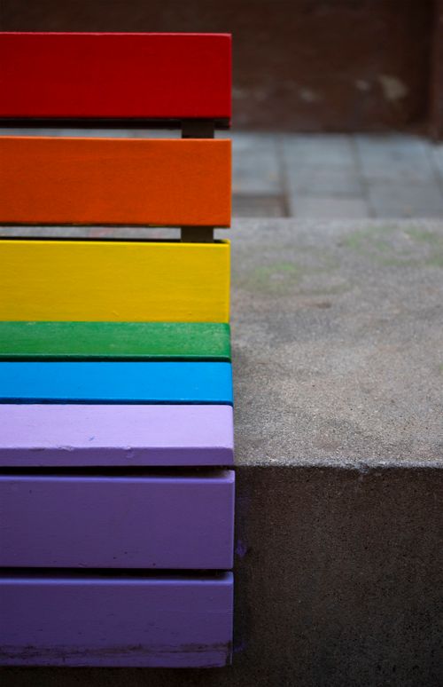 Free A close-up of a vibrant rainbow-colored wooden bench against a concrete background. Stock Photo