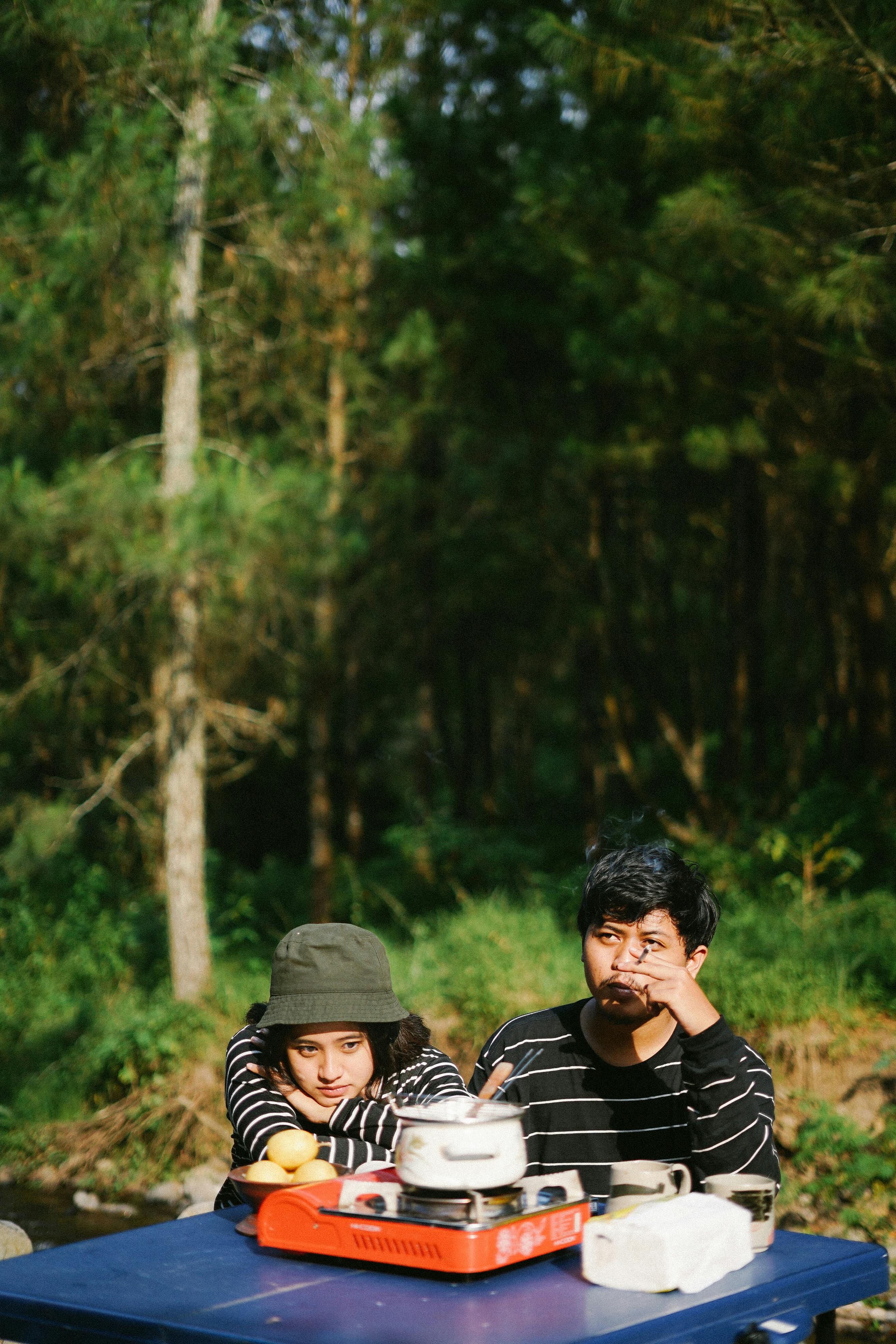 A couple enjoying cooking at a campsite in a serene forest environment.