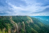 在阴云密布的天空下，一道雄伟的瀑布从郁郁葱葱的绿色悬崖上倾泻而下
