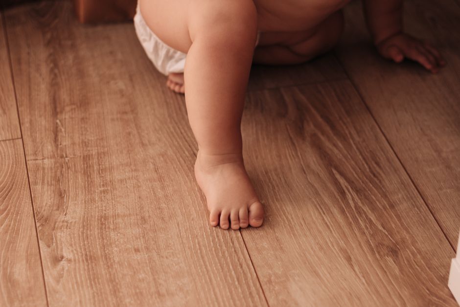 Close-up of a baby crawling indoors on a wooden floor, showcasing tiny feet and playful innocence.