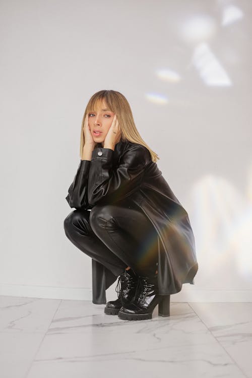 Woman in Black Leather Jacket and Black Pants Sitting on White Floor