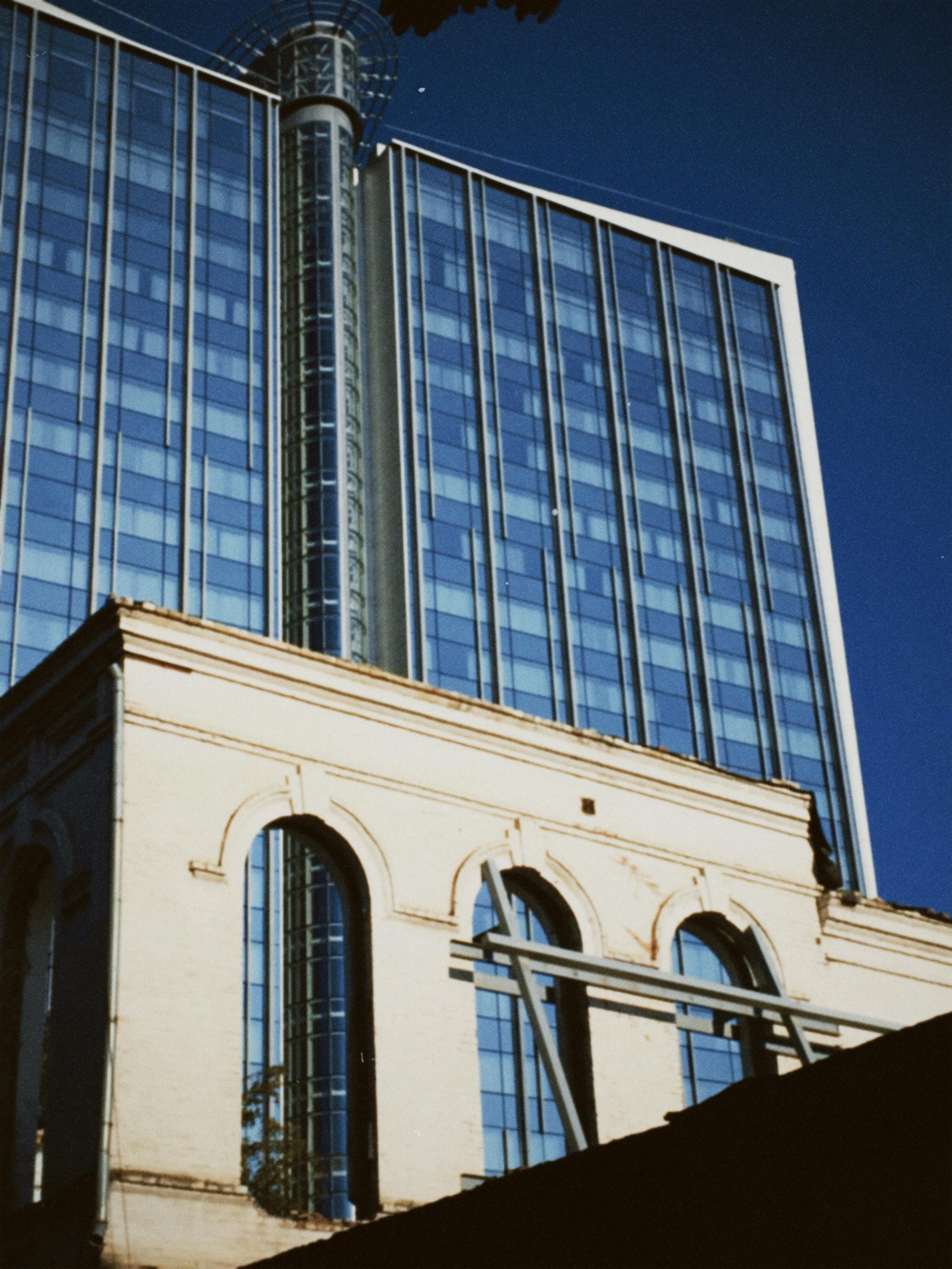 Contemporary glass skyscraper juxtaposed with an old architectural facade, capturing urban contrast.