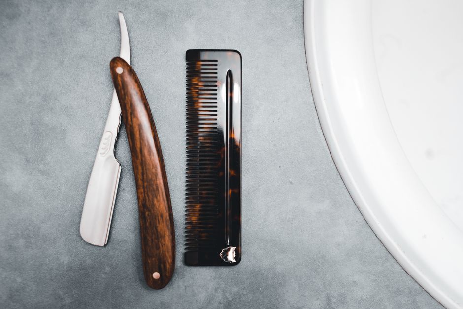 Top view of a razor and comb on a stylish gray surface, creating a modern grooming theme.