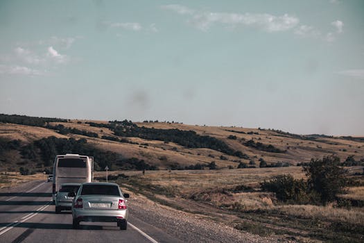 A rural road with vehicles driving through a scenic countryside landscape under a clear sky.