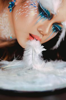 A woman with creative blue fantasy makeup and feathers, showcasing artistic expression.