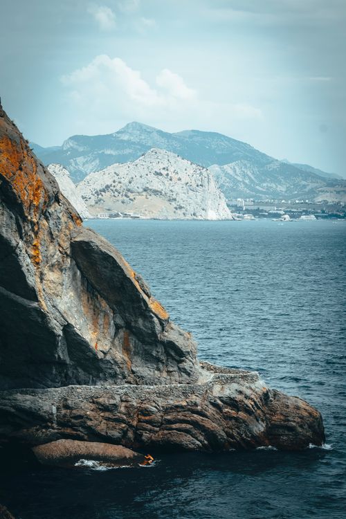Free Breathtaking view of a coastal cliff and serene sea set against stunning mountains. Stock Photo
