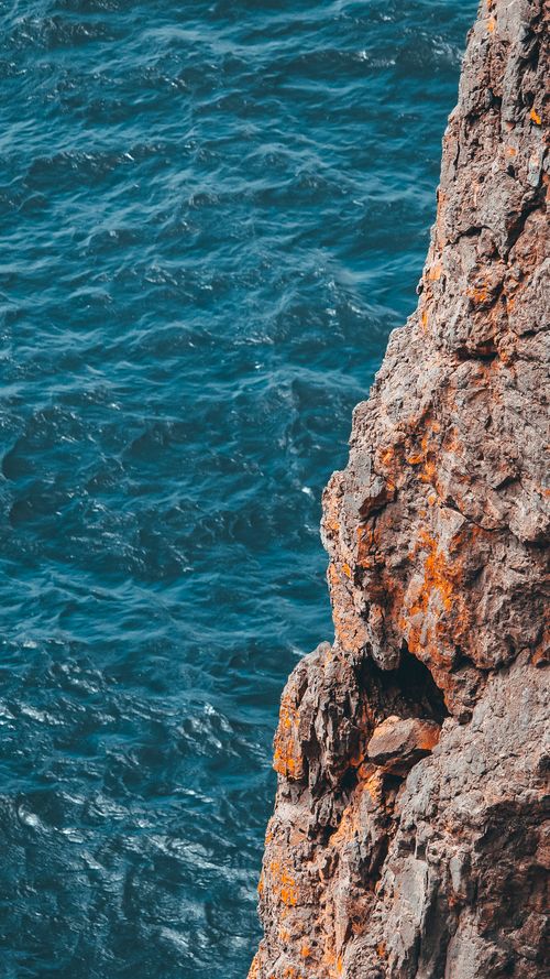 Free A stunning vertical shot of a cliffside with vibrant blue sea in the background, showcasing nature's beauty. Stock Photo