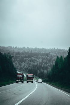 Wide view of trucks traveling on a forest road under overcast skies. Ideal for backgrounds.