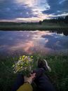 A Person Sitting on Green Grass Near the Lake while Holding a Bunch of Flowers
