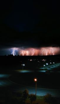 Dramatic view of lightning illuminating the night sky during a thunderstorm over a city road.