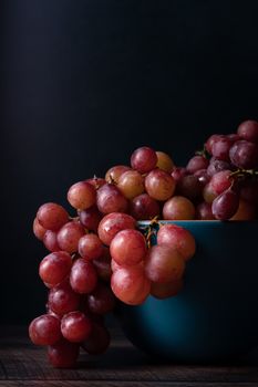 Fresh red grapes cascading over a blue bowl against a dark backdrop.