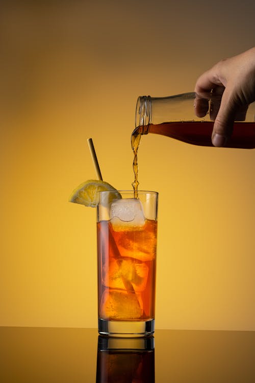 Person Pouring Brown Liquid on Drinking Glass 