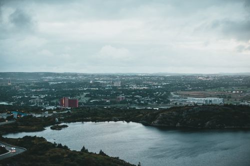 Free A sweeping aerial shot of a city landscape with a serene lake under a cloudy sky. Stock Photo